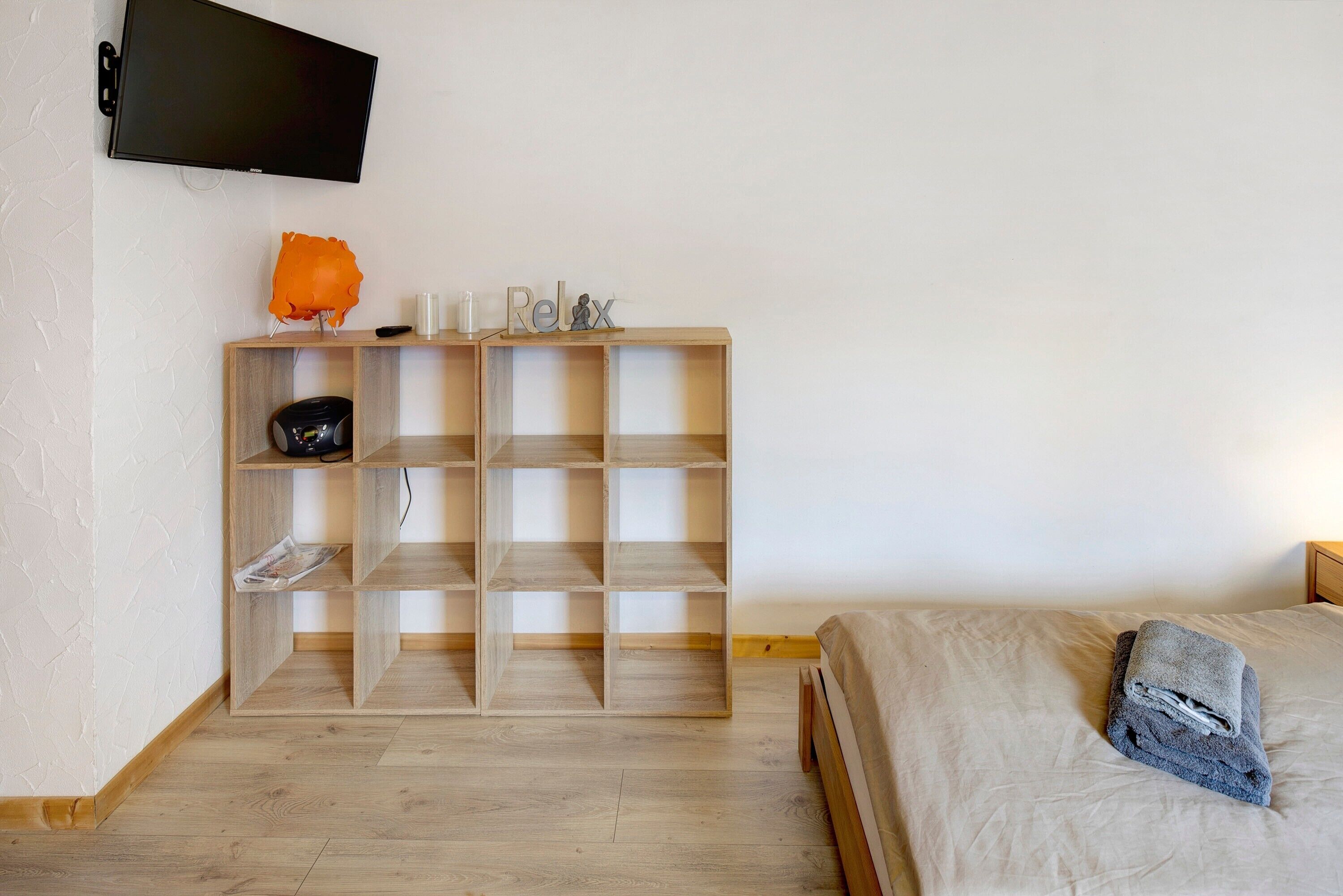 Ein Schlafzimmer mit Bett, einem Holzschrank, einem Flachbildfernseher und einem Regal mit Dekoration.