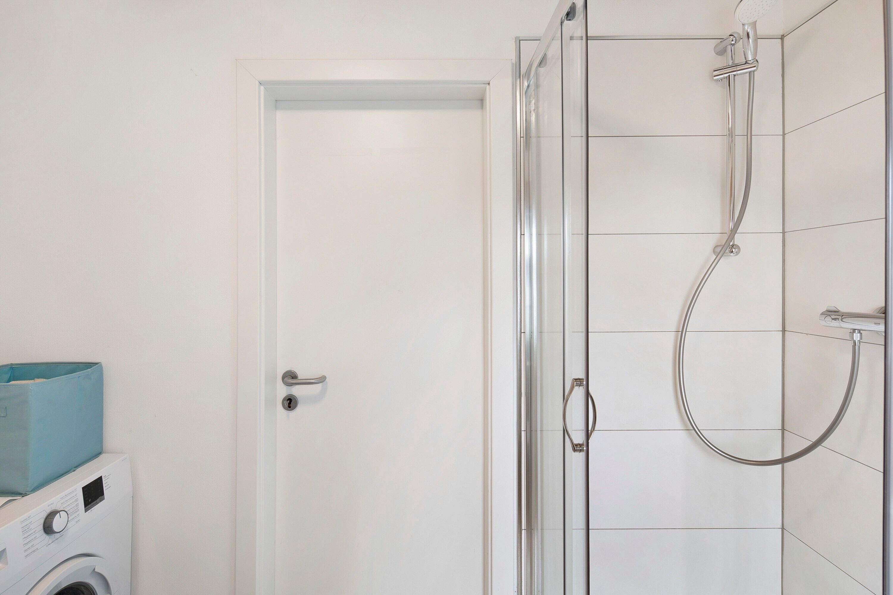 A bathroom with a glass-enclosed shower, a washing machine, and a door.