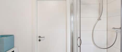 A bathroom with a glass-enclosed shower, a washing machine, and a door.