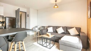 A modern living room with a grey sofa, a wooden coffee table, and a dining area with a black chair and a grey table.
