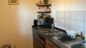 A compact kitchen with a stove, sink, and wooden cabinets. There is a trash bin and a hanging light fixture. - Ferienwohnung bis 4 Personen (Kiefersfelden)