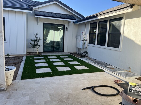Un immobile residenziale con patio in pietra, una piccola area verde e un portone garage.