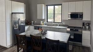 Een moderne keuken met witte kastjes, roestvrijstalen apparatuur, een marmeren aanrechtblad en een groot raam.