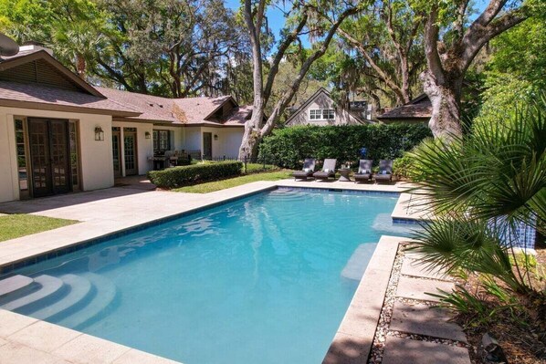 A swimming pool with lounge chairs, surrounded by trees and a house. - Beautiful Family Home Located Near Sea Island (Saint Simons Island)