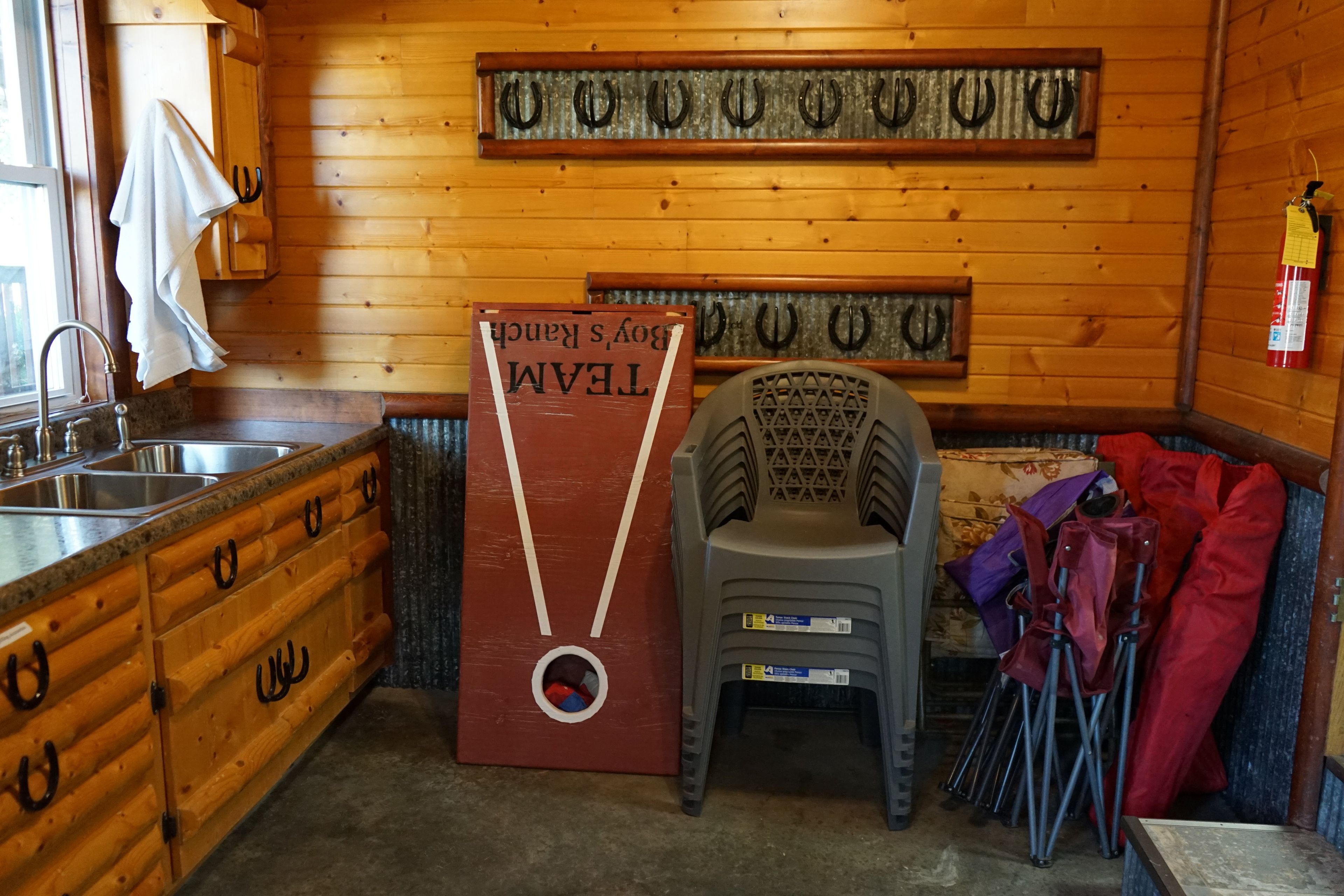 L’intérieur d’un chalet en bois comprend un coin cuisine, un grand meuble en bois muni de crochets, une petite chaise et un extincteur fixé au mur.