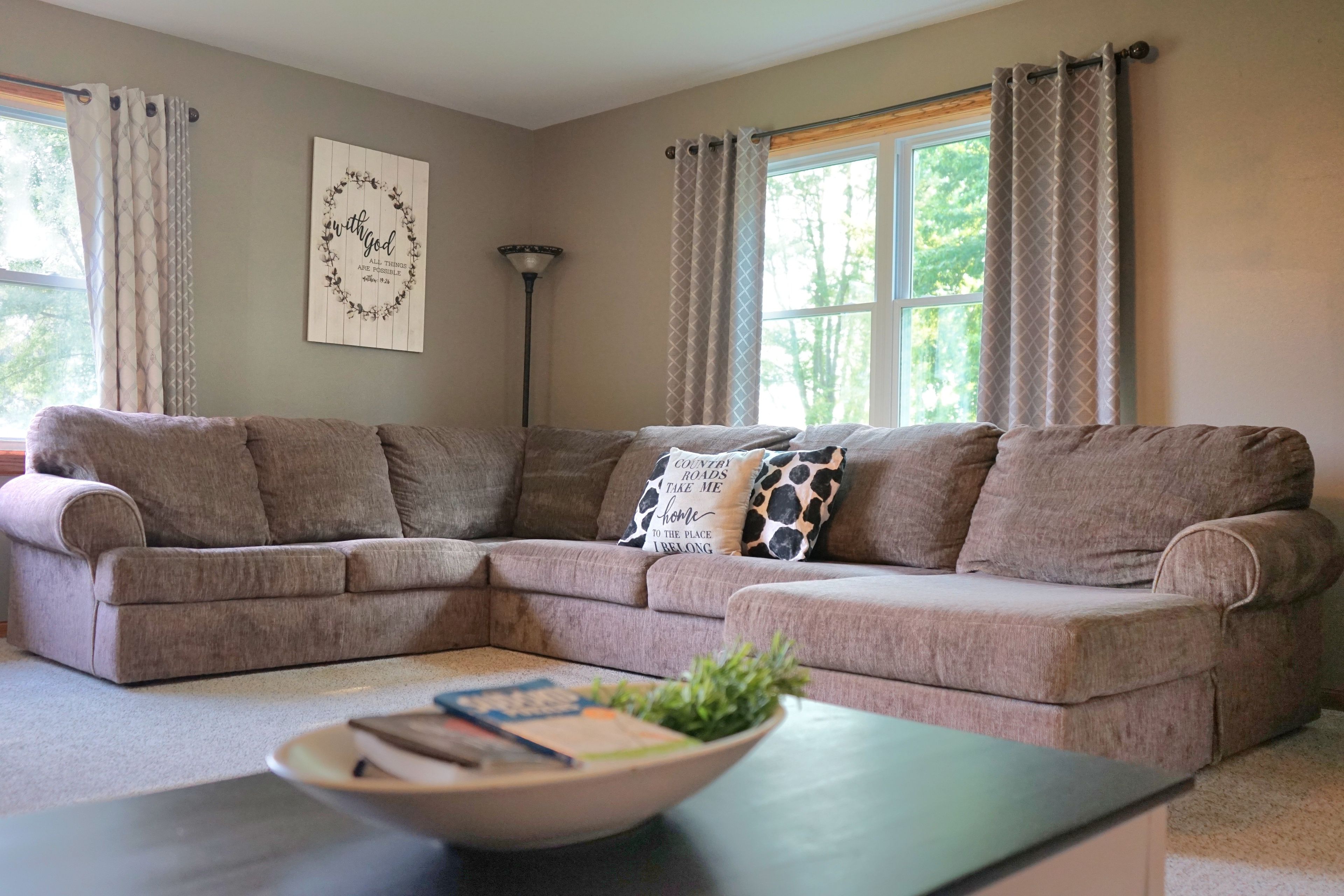 A living room with a sectional sofa, a coffee table with books and a plant, and a wall with a motivational quote.