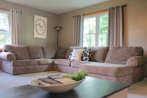 A living room with a sectional sofa, a coffee table with books and a plant, and a wall with a motivational quote.
