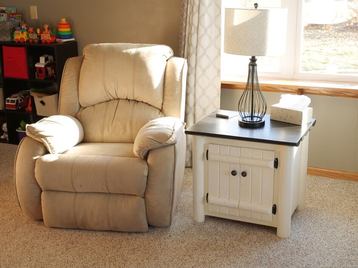 A beige armchair next to a white cabinet with a lamp on top.