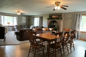 A dining area with a wooden table and chairs, a fireplace, and a ceiling fan.