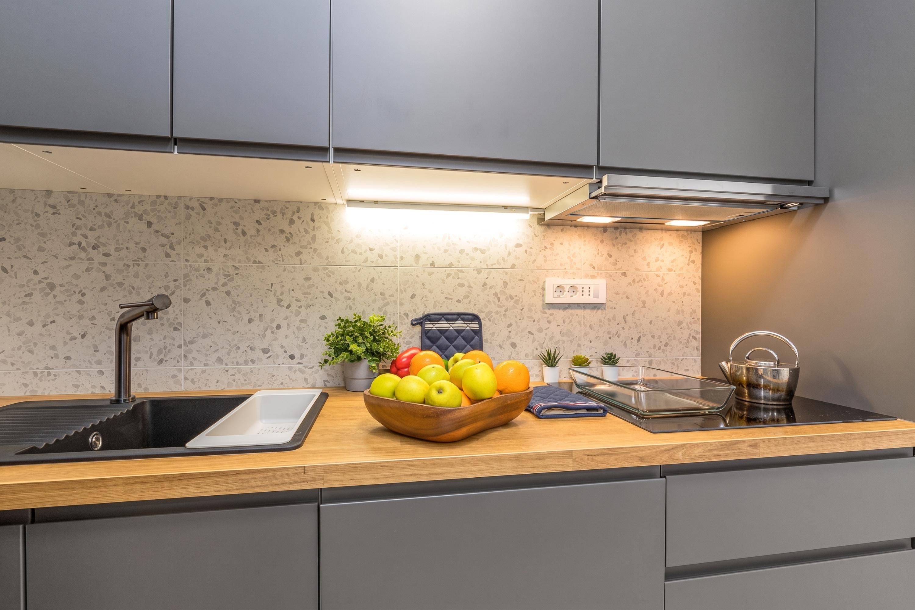 Una cocina moderna con encimera de granito, pileta de acero inoxidable y un bol con fruta.
