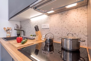 Una cocina moderna con una encimera negra, un hervidor de acero inoxidable, una olla, una tabla de cortar con verduras y un bloque para cuchillos.
