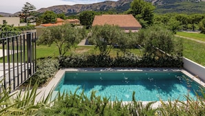 A swimming pool with a view of mountains, surrounded by greenery and a building with a red roof.