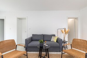 Un salon moderne avec un canapé gris, deux fauteuils en osier, une petite table ronde et un vase contenant des plumes d’herbe des pampas.