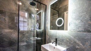 Ein modernes Badezimmer mit einer Duschkabine aus Glas, einem weißen Waschbecken und einem großen Spiegel mit integrierter Beleuchtung.