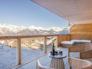 A balcony with a view of snow-covered mountains, wicker furniture, and a bottle of wine.