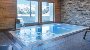 A modern indoor pool with a stone wall and wooden paneling, large windows offering a mountain view. - Les Terrasses de Nendaz D1 by Interhome (Nendaz)