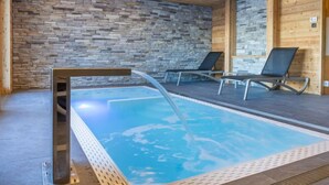 A modern indoor swimming pool with stone walls and wooden beams, equipped with two lounge chairs. - Les Terrasses de Nendaz D1 by Interhome (Nendaz)
