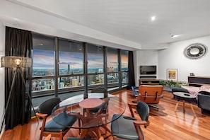 Enjoy the stunning city view from the comfort of this stylish living room, featuring a sofa, flat-screen TV, and dining area.
