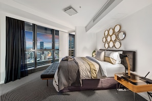 Enjoy a city view from the comfort of a spacious bed, accompanied by a desk and wall-mounted mirror.
