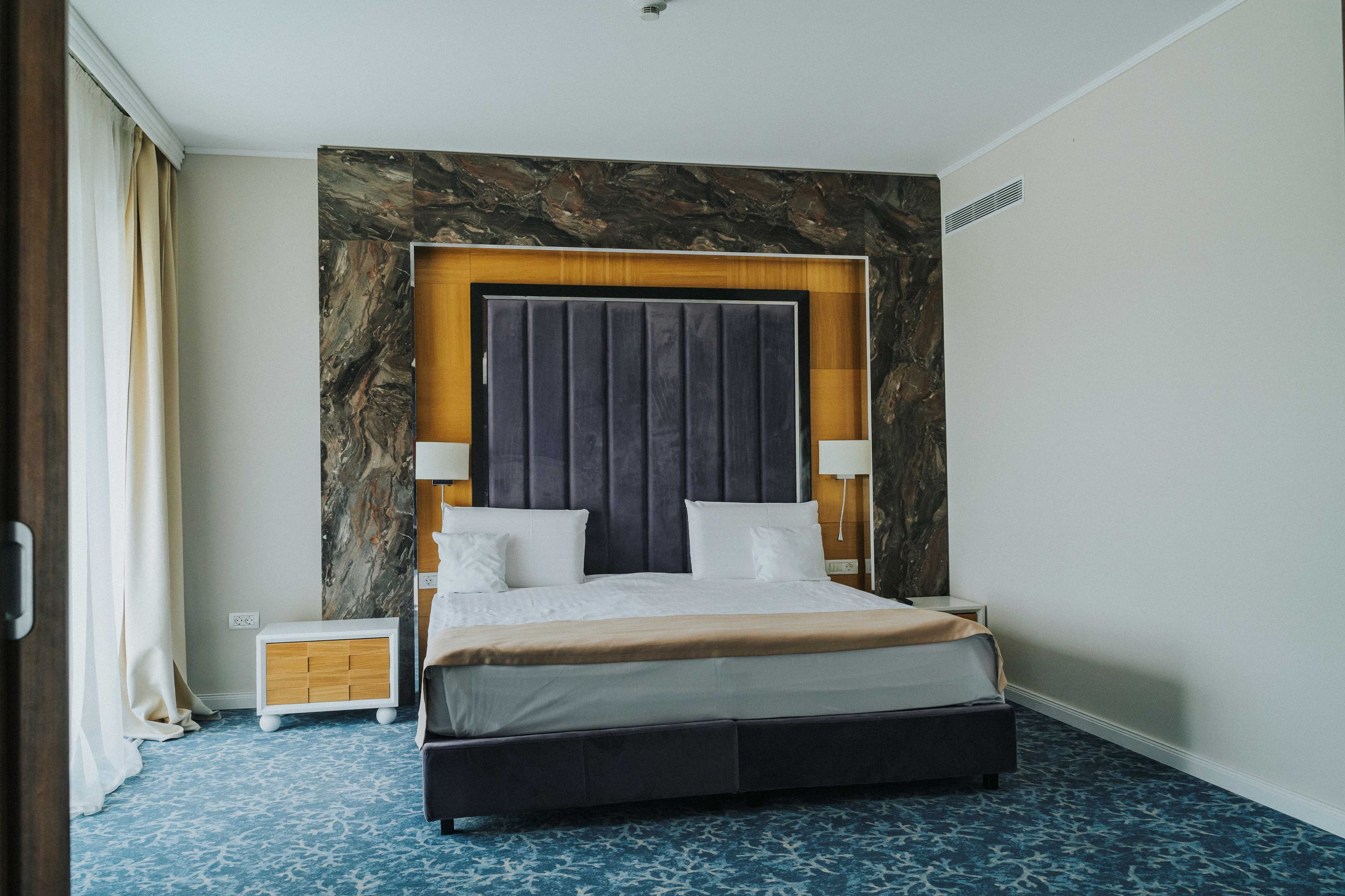 Una habitación de hotel moderna con una cama grande, cabecera de madera, una mesita de noche y una pared de acento de mármol.