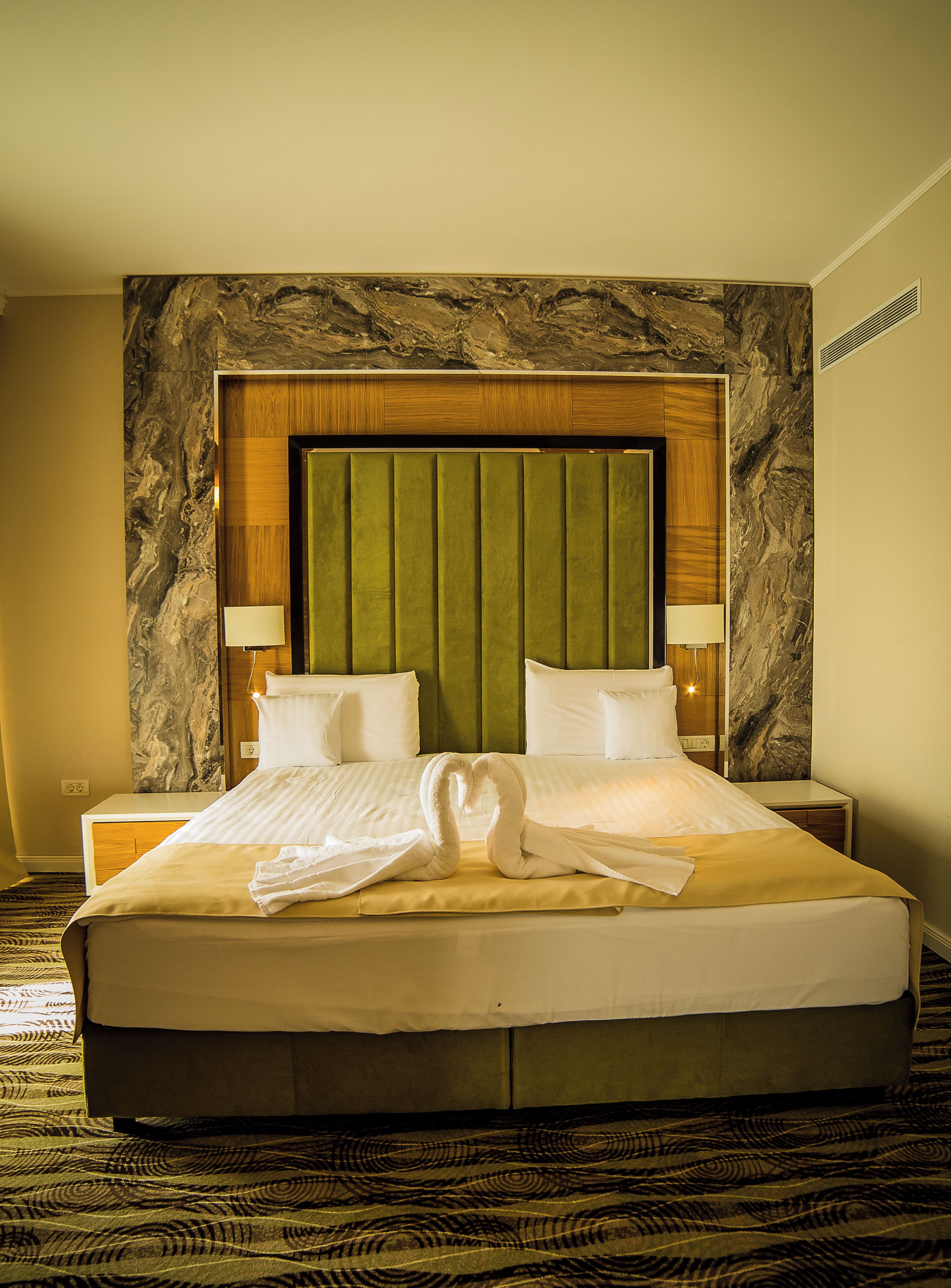 A hotel room with a large bed, two bedside tables, a headboard with a marble-like design, and a green upholstered headboard panel.