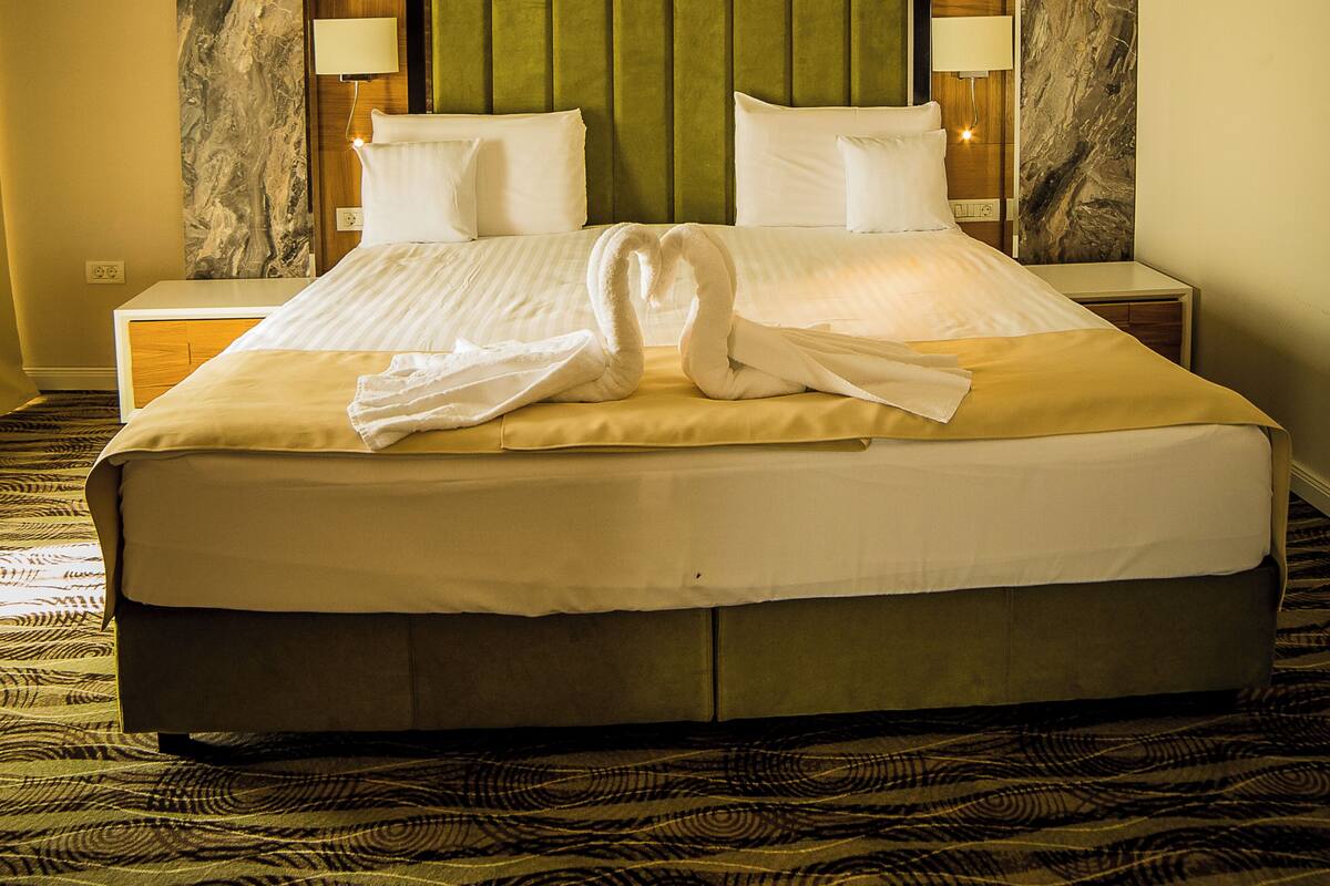 Una habitación de hotel con una cama grande, dos mesitas de noche, un cabecero con diseño tipo mármol y un panel tapizado en verde para el cabecero.