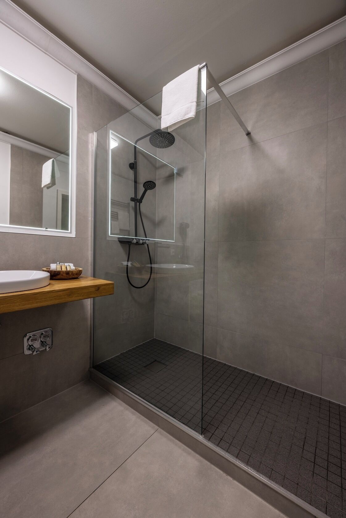 Ein modernes Badezimmer mit einer gläsernen Duschkabine, einem Holzbadezimmer-Möbelstück mit Waschbecken und einem Spiegel.