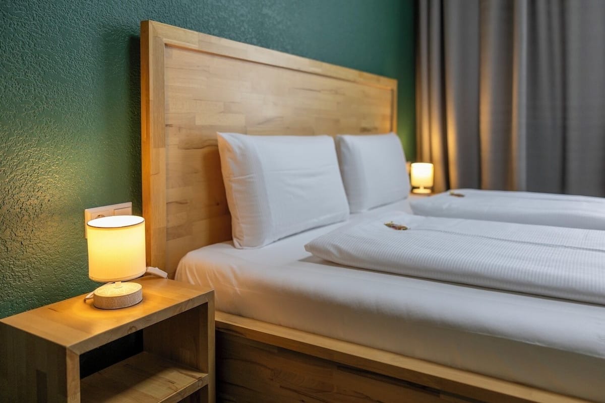 A double bed with a wooden headboard, white bedding, and a bedside lamp.