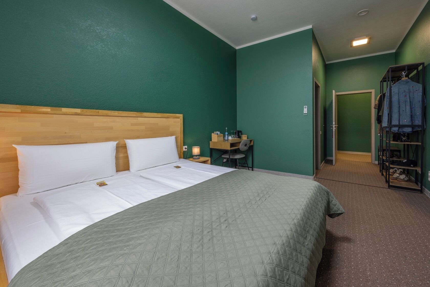 Habitación de hotel con cama, escritorio con silla, armario y una puerta que da a otra habitación.