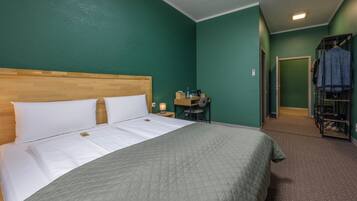 Habitación de hotel con cama, escritorio con silla, armario y una puerta que da a otra habitación.