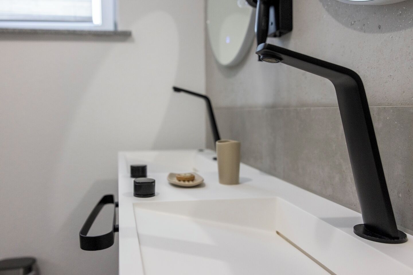 Une salle de bain moderne avec un lavabo blanc, un robinet noir et un petit récipient de couleur beige.