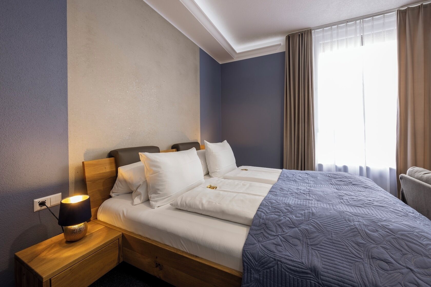 A hotel room with a bed, bedside lamp, and a window with curtains.