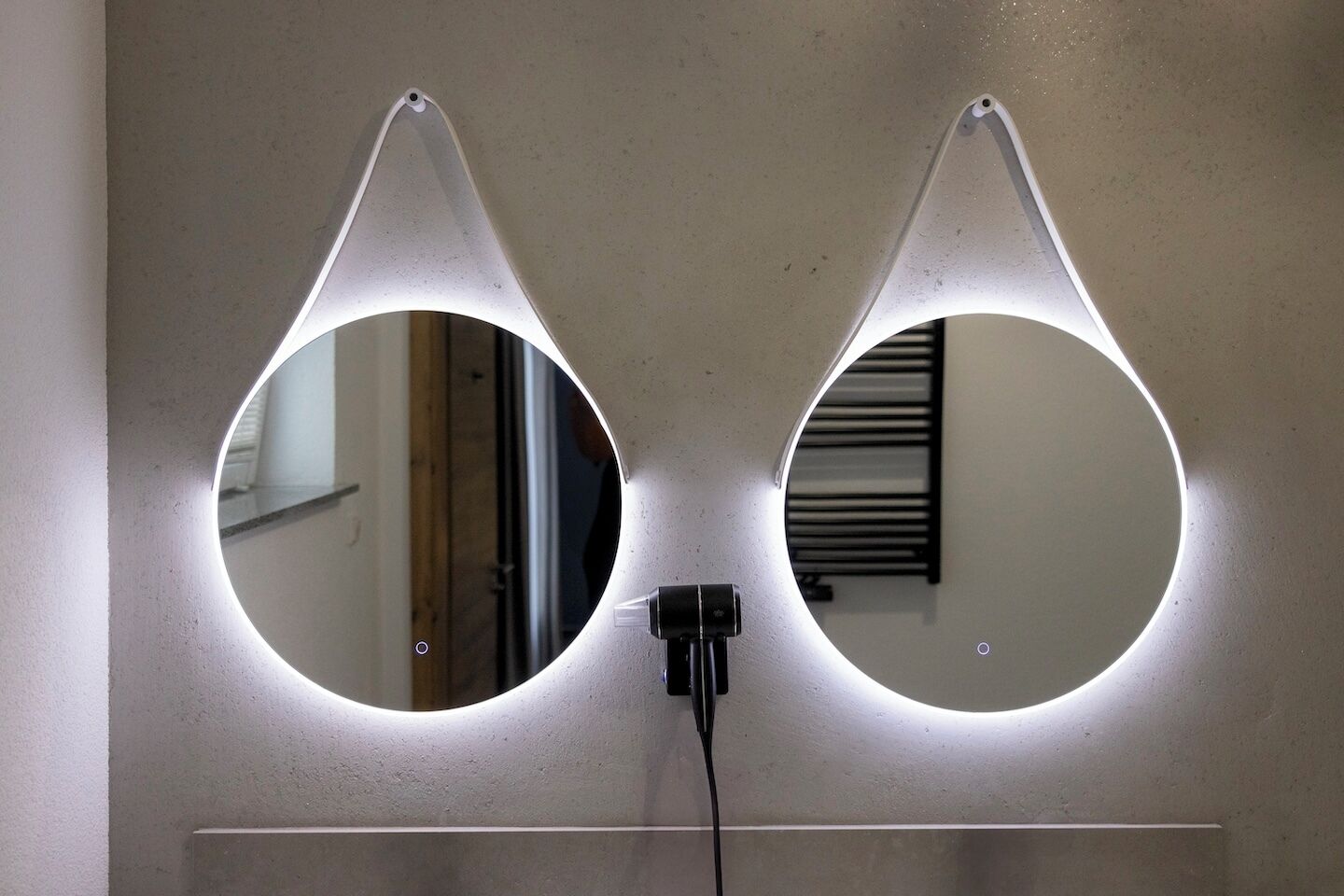 Deux miroirs rétroéclairés sont fixés au mur, et une prise de courant se trouve en dessous.