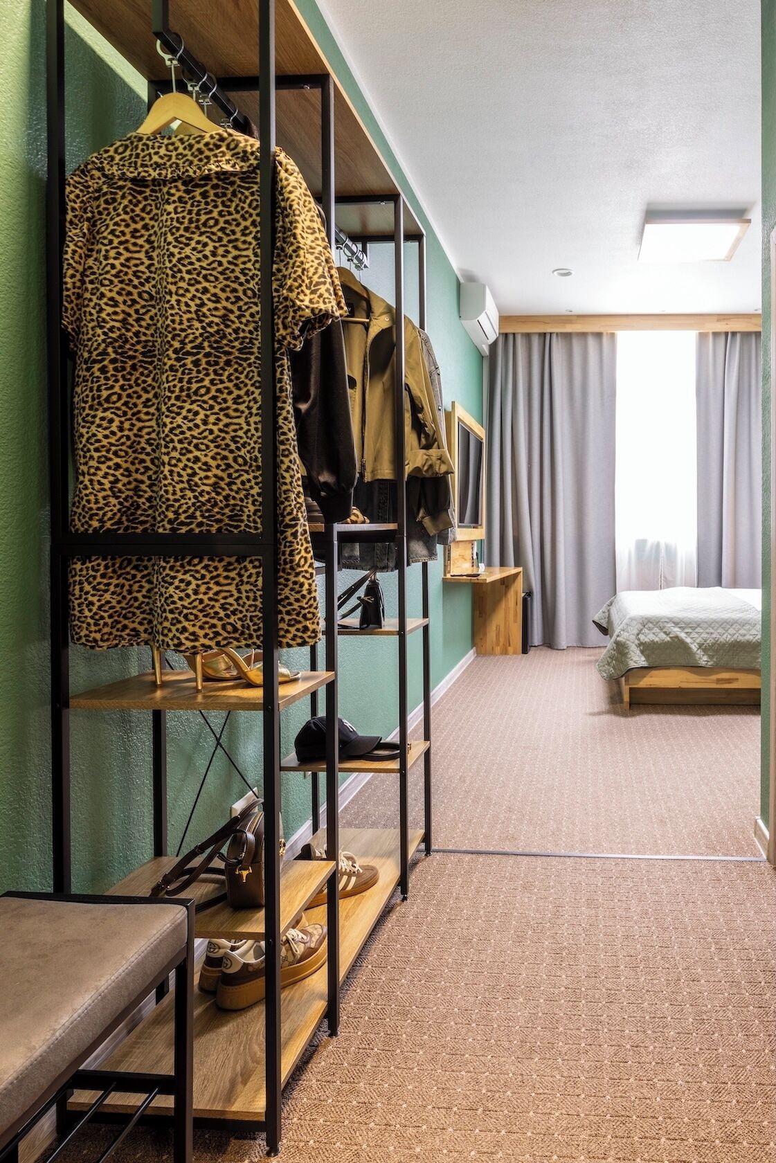 A hotel room with a bunk bed, a wardrobe with a leopard print cover, a wooden bench, and a bedside table with a lamp.