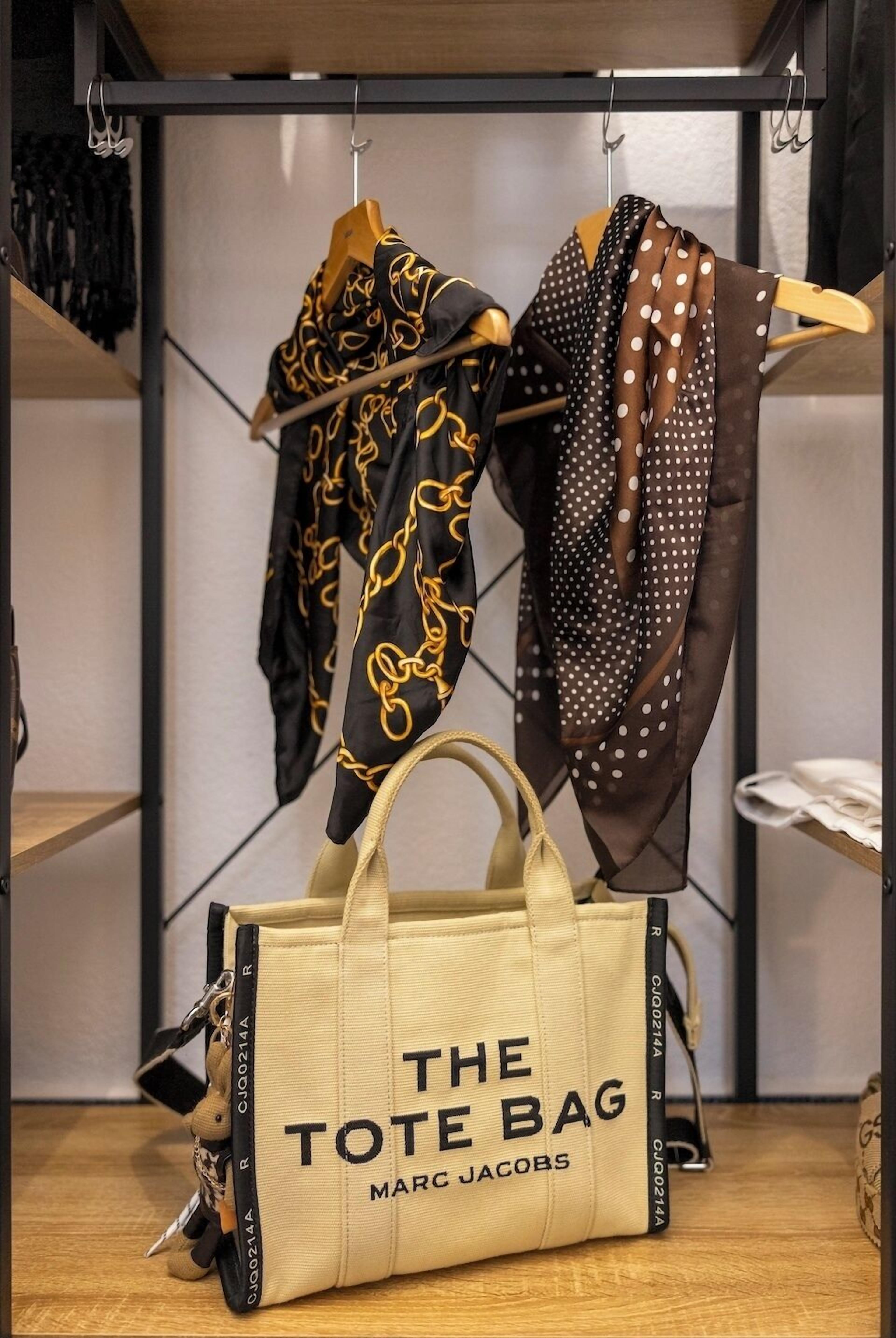 A Marc Jacobs tote bag labeled "THE TOTE BAG" on a shelf.
