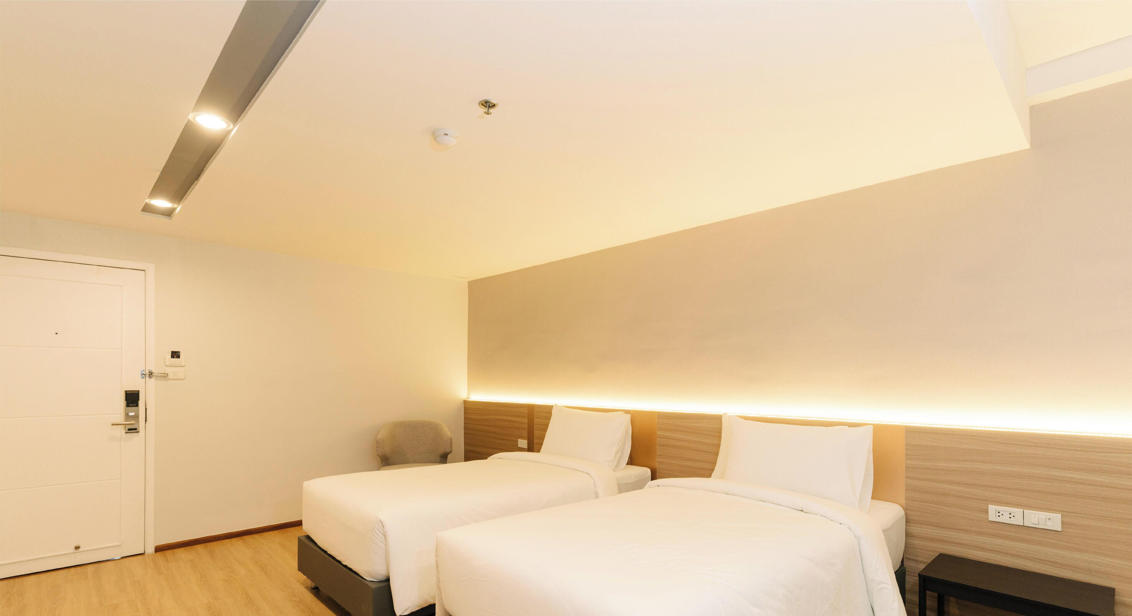 Habitación de hotel con dos camas, un escritorio, una silla, una puerta y una lámpara en el techo.