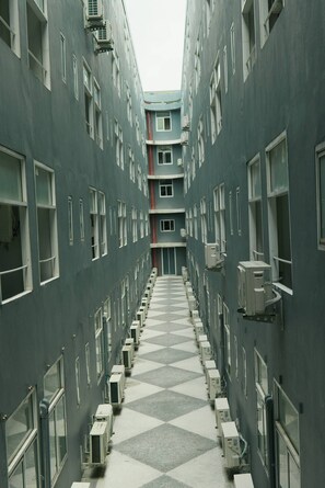 A corridor with a checkered floor, flanked by air conditioning units and windows. - Le Srivaree Suvaranabhumi Airport Hotel (Bang Phli)