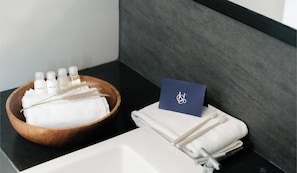 A hotel bathroom with a wooden bowl containing toiletries, a folded towel, and a card on the counter. - Le Srivaree Suvarnabhumi Airport Hotel (Bang Phli)