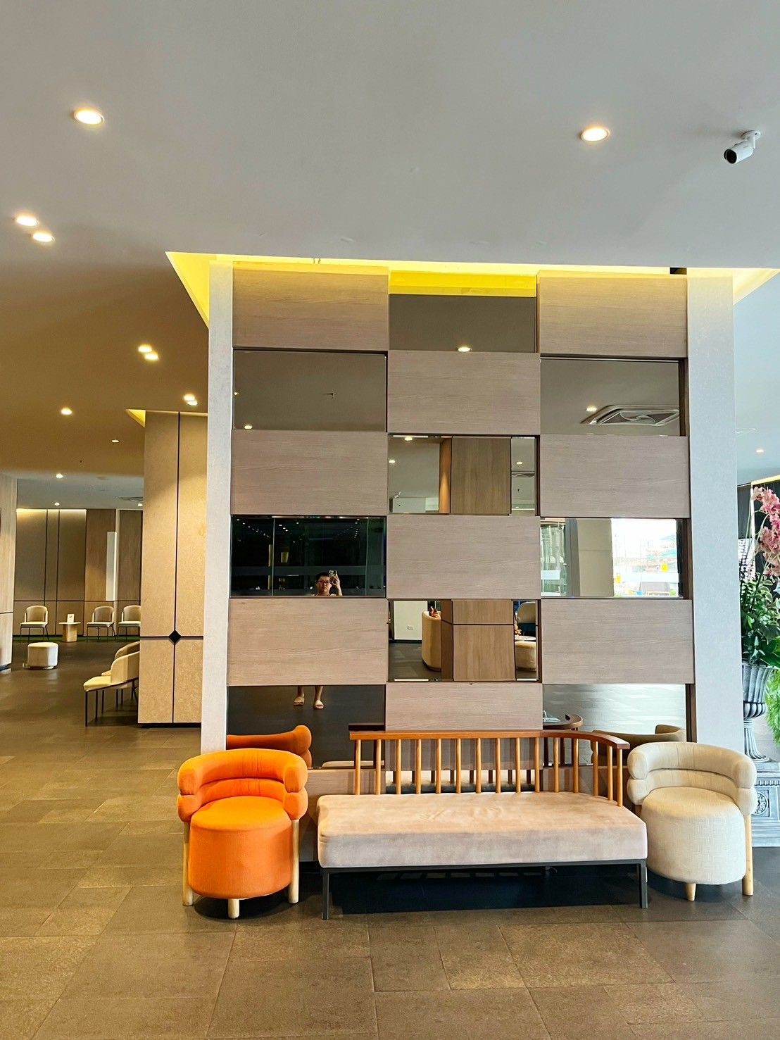 A modern lobby with a seating area, a large wall with a reflective surface, and a ceiling with recessed lighting.