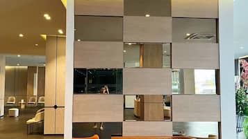 A modern lobby with a seating area, a large wall with a reflective surface, and a ceiling with recessed lighting.