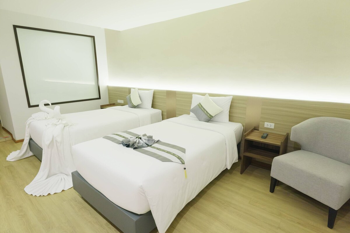 Hotellihuone, jossa on kaksi sänkyä, tuoli, kylpytakki ja suuri peili.