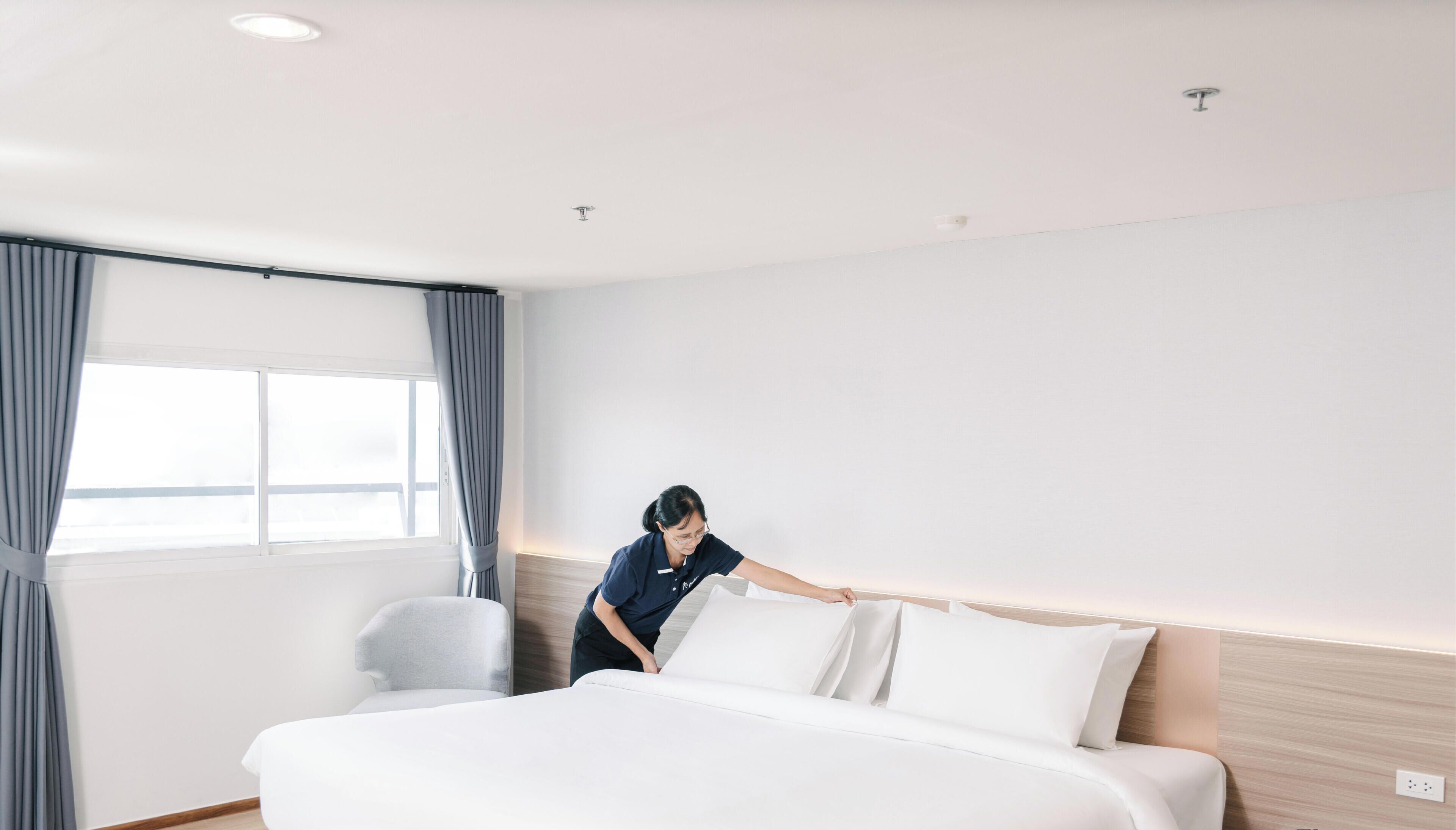 Una habitación de hotel con una cama bien hecha, una ventana con cortinas y un cabecero de madera.