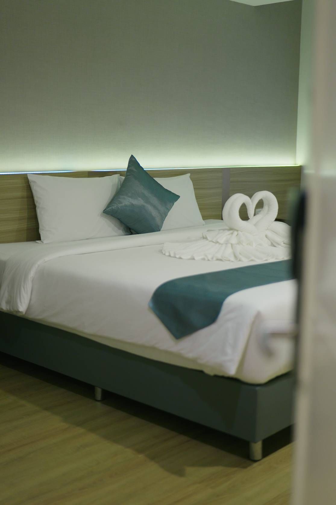 A neatly made bed with white linens and a teal throw blanket, a pillow, and a decorative swan-shaped towel.