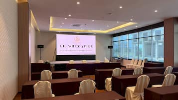 A conference room with a stage, rows of tables, and chairs, and a large screen displaying 'LE SRIVAREE'.