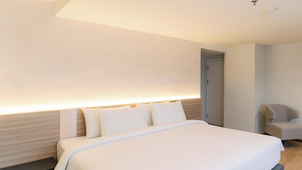 A modern hotel room with a large bed, a wooden headboard, a bedside table, and a chair. - Le Srivaree Suvaranabhumi Airport Hotel (Bang Phli)