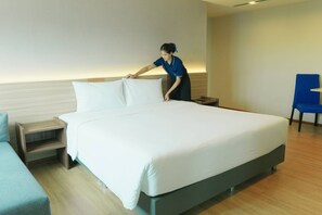 A hotel room with a large bed, a bedside table, a chair, and a wall-mounted light.