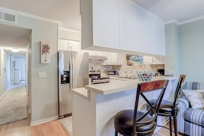 A modern kitchen with white cabinetry, a central island, and a dining area with striped upholstered chairs.