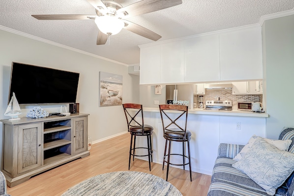 A living room with a TV, two bar stools, a sofa, and a ceiling fan.