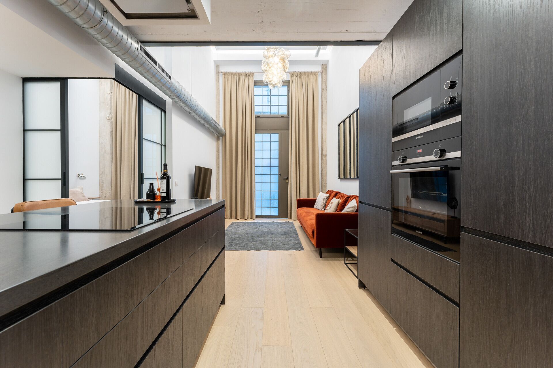 Een moderne keuken met donkere houten kastjes, een inbouwoven en een eethoek met een glazen tafel en stoelen.