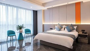 Habitación de hotel moderna con una cama grande, una mesita con sillas, una planta en maceta y una mesita de noche.